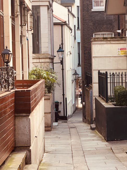 A quiet residential street in Holland Park with traditional terraced houses featuring brick and white-painted facades, small front gardens with potted plants, and external balconies with black metal r