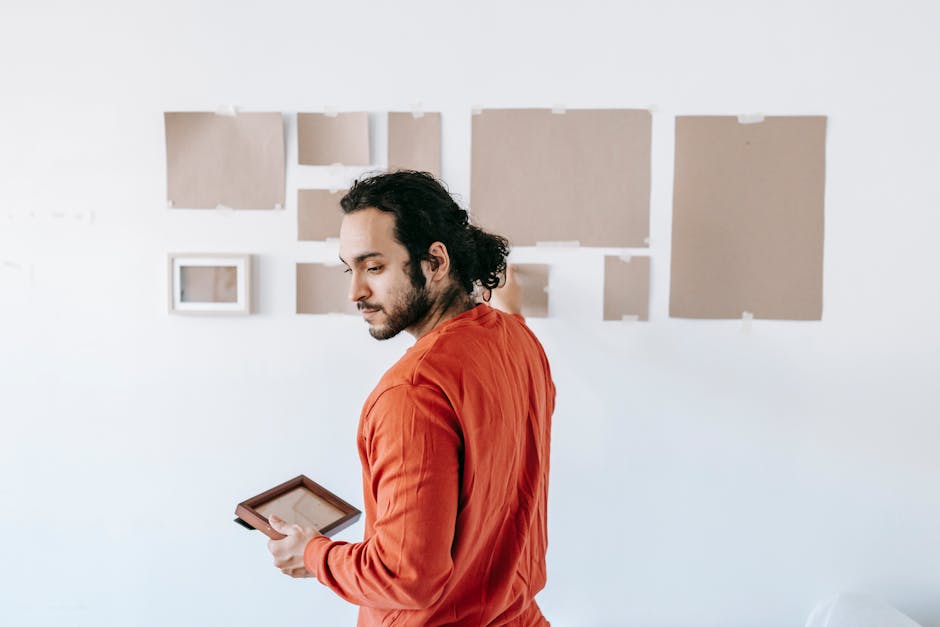 A collection of framed artwork and paintings in various sizes and ornate frames, leaning against each other in a storage or preparation area. The images include landscapes, cityscapes, and portraits,